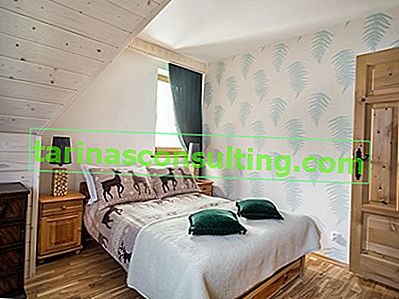dřevěný noční stolek, zelený polštář, bílý přehoz na postel, kapradinová tapeta